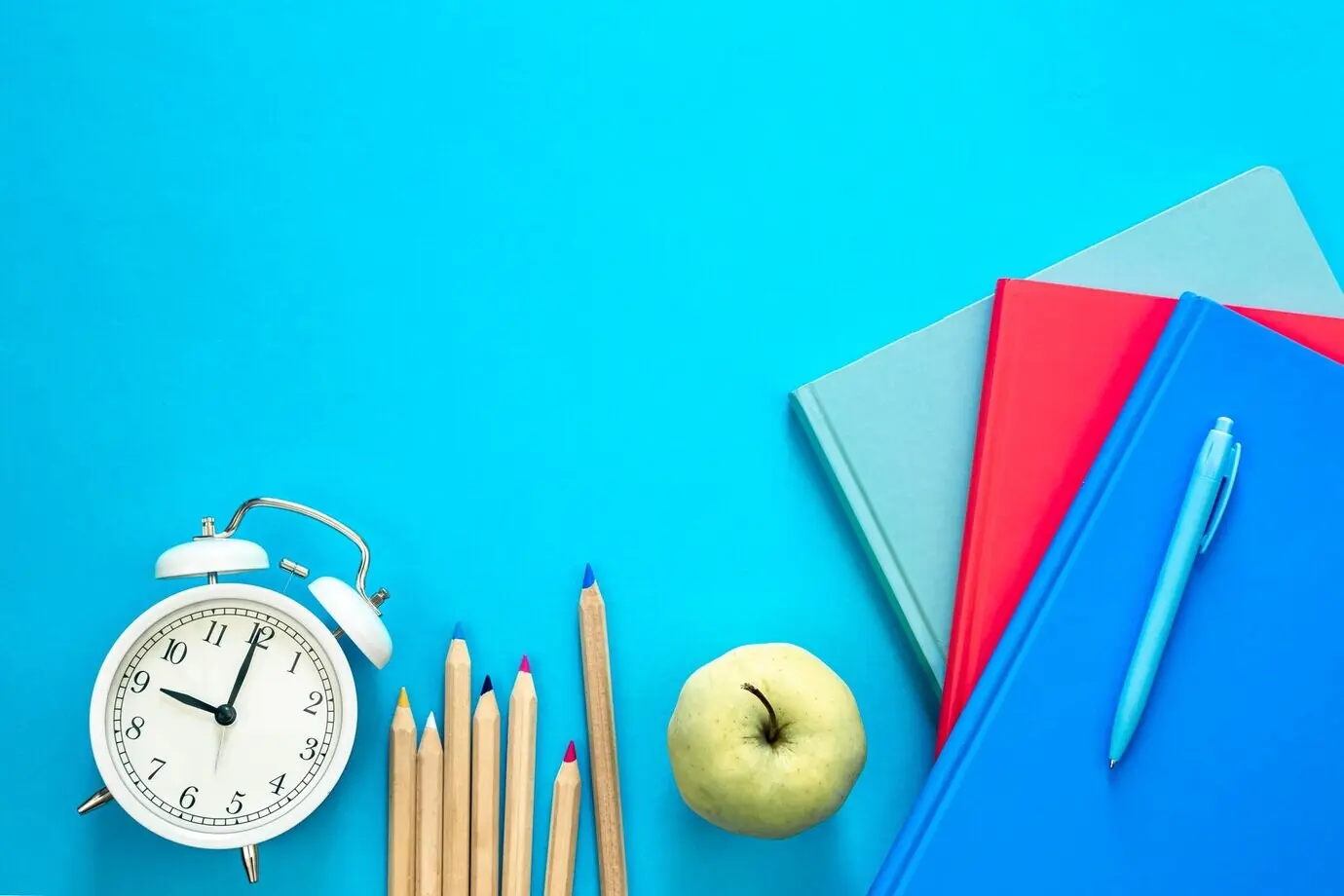 Komposition in Draufsicht mit bunten Schulmaterialien auf blauem Hintergrund.